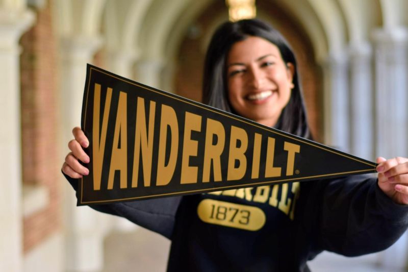 Miti Joshi holding a Vanderbilt pennant in an arched walkway.